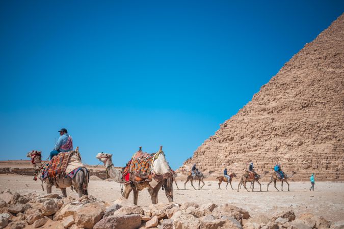 People riding camels on brown sand beside pyramid of Giza, El Omraniya, Giza Governorate, Egypt 
