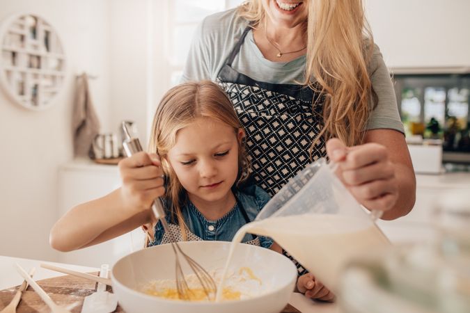 Cute little girl and her mother mixing batter in the bowl