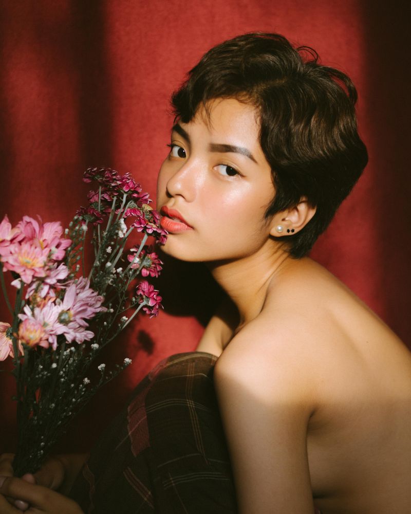 Topless woman beside flower vase against red background