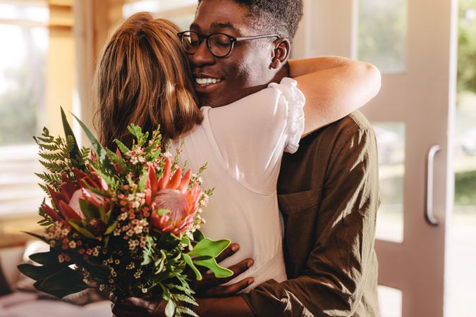 Young man giving woman flowers and hugging her