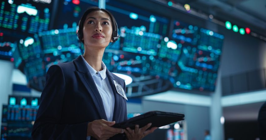 Female Investment Banker Wearing Headphones and Using a Tablet Computer with Financial Market Analytics Data.