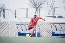 Black soccer player with red outfit playing soccer.