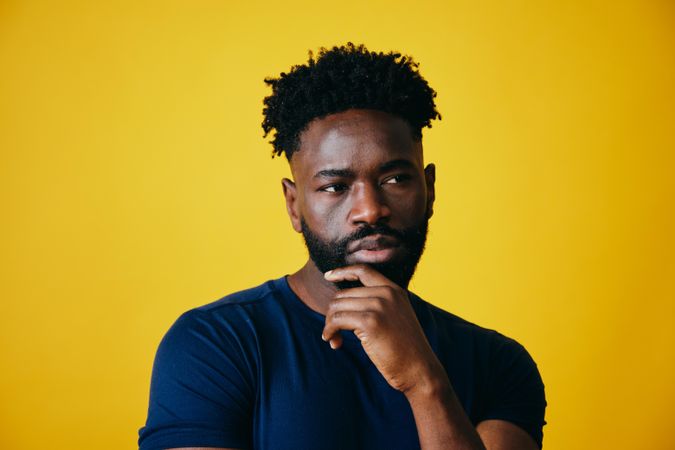 Portrait of Black man contemplating with hand to chin on yellow background