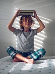 Little boy putting pile of books on head