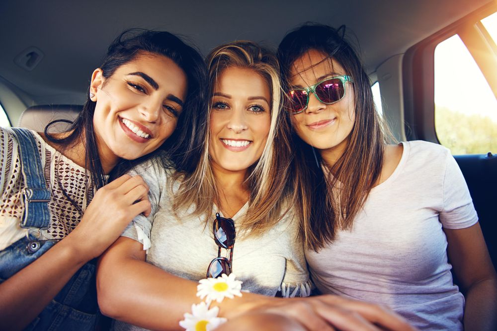 Group of happy female friends talking with each other while riding in back of vehicle