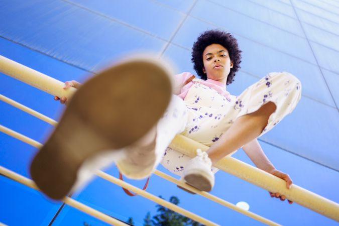 Low angle shot of woman sitting on handrails in front of  reflective glass building on sunny day