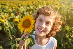 Cheerful boy with sunflower growing in field on sunny day