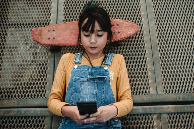 Girl with smartphone and skateboard lying on walkway