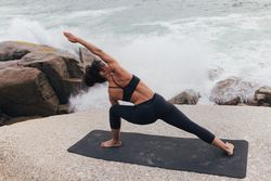 Female stretching her side with arm up in yoga pose while next to the ocean