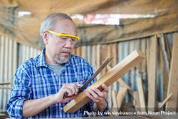 Asian male carpenter using ruler on wooden panel 5kRR3D