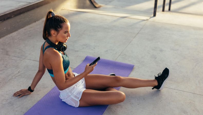 Female sitting on exercise mat with a mobile phone outside