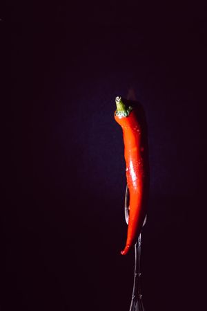 red chili pepper on fire in fork on a dark background