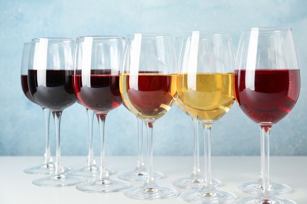 Glasses with different wine on table against light blue background