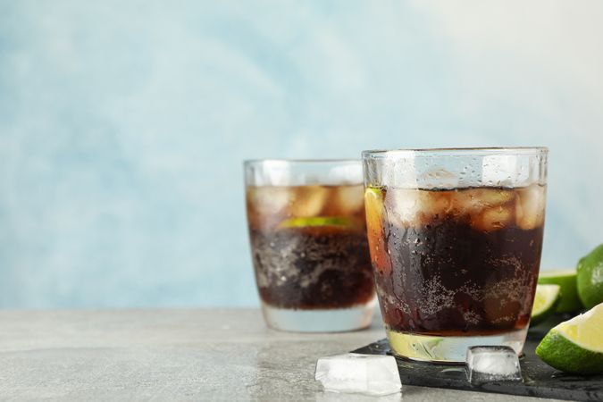 Glasses with cold cola and citrus on grey table, space for text