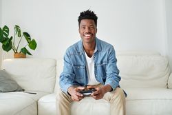 Happy Black man with game pad playing on sofa