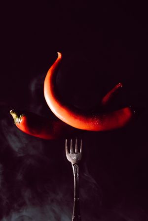two red chili pepper in fork on a dark background with smoke