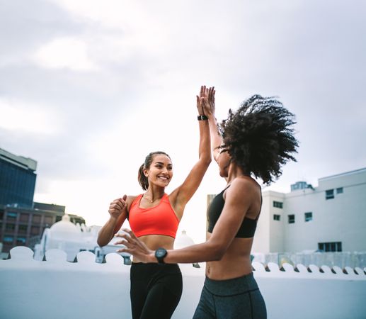 Two cheerful women in fitness wear giving high five while running on the terrace