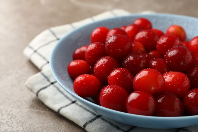 Bowl with red cherry and towel on gray background, close up