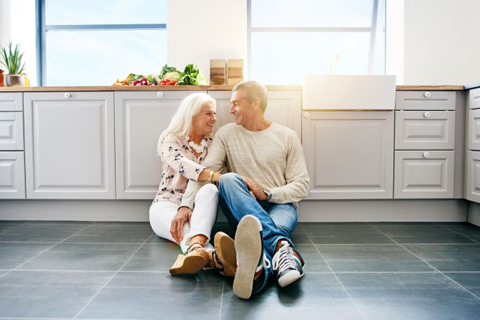 Smiling older couple looking at each other while seated on kitchen floor