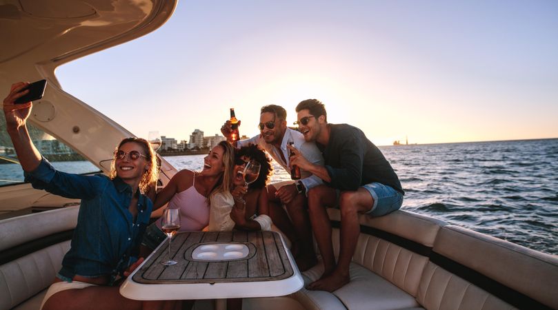 Group of men and woman relaxing on yacht with drinks and taking selfie