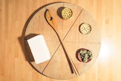 A bread board with a grinder, dried marijuana, spatula and butter