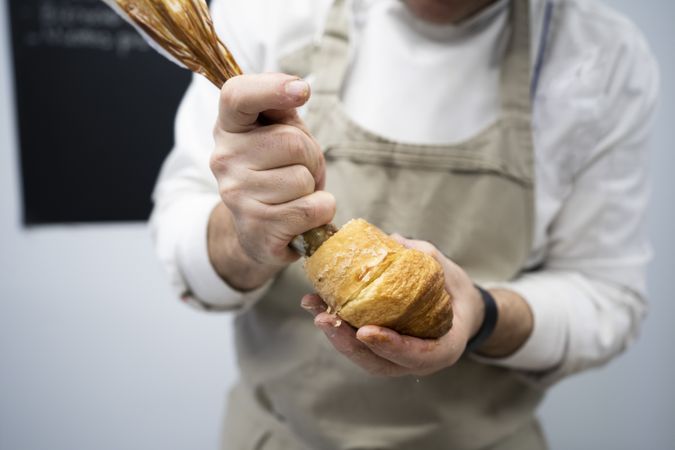 Confectioner pouring chocolate filling into croissant