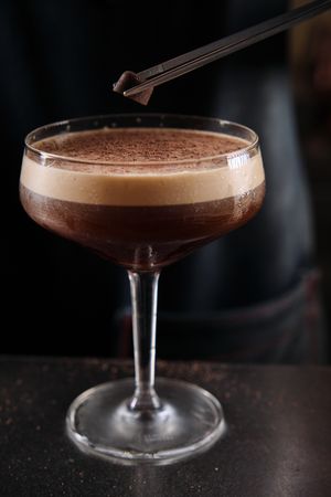 Barman garnishing espresso martini cocktail with chocolate