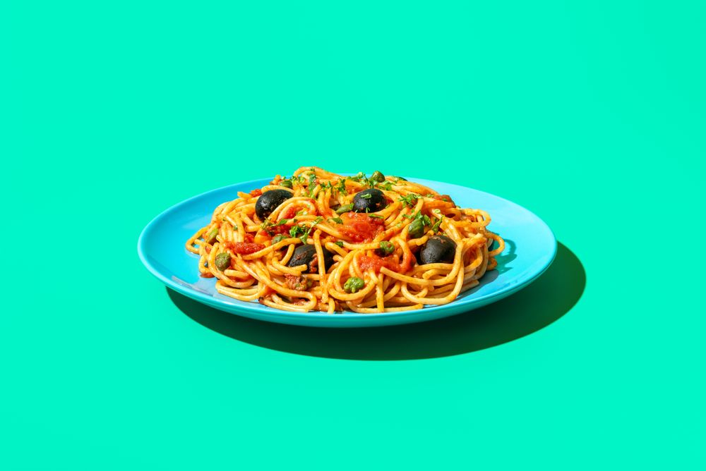 Spaghetti puttanesca plate in bright light, minimalist on a green background