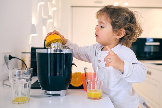 Adorable kid making orange juice in kitchen