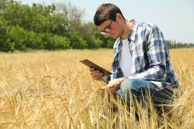Young man with clipboard in barley field. Agriculture business