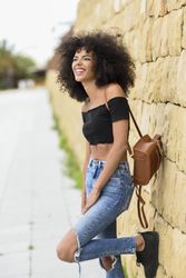 Happy female standing on street with one leg up leaning on wall