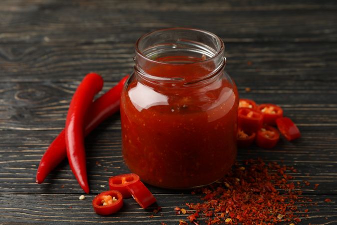 Chilli pepper and glass jar of sauce on wooden  background