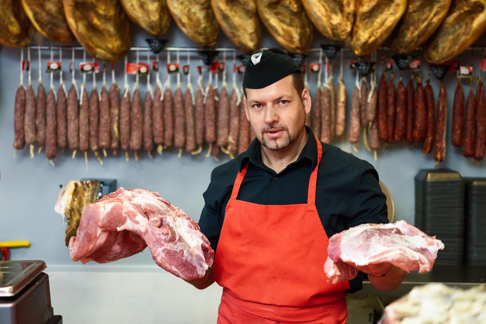 Man holding chunks of ham behind counter in butcher shop