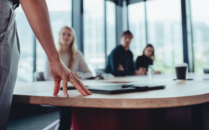 Focus on hand of businesswoman on table while talking with colleagues in boardroom