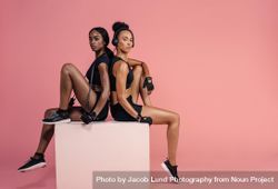 Female friends sitting on a box and looking at camera 56qqL0