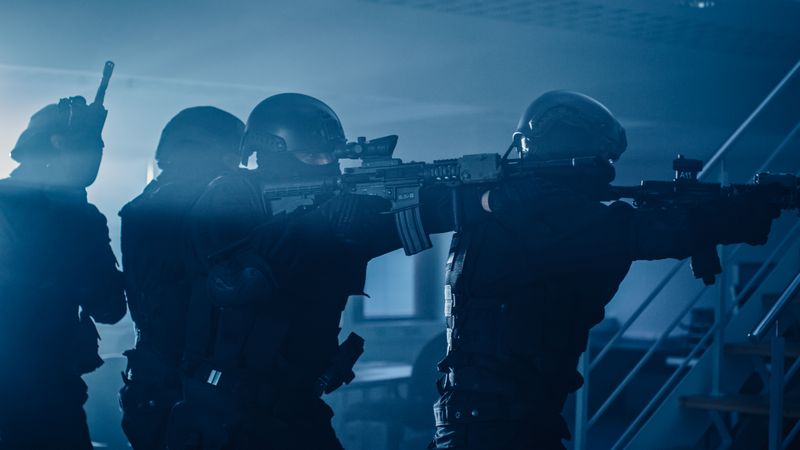 Masked Squad of Armed SWAT Police Officers Move in a Hall of a Dark Seized Office Building with Desks and Computers.