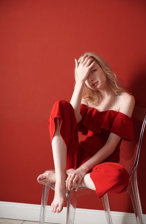 Beautiful young adult woman wearing red jumpsuit relaxing in studio