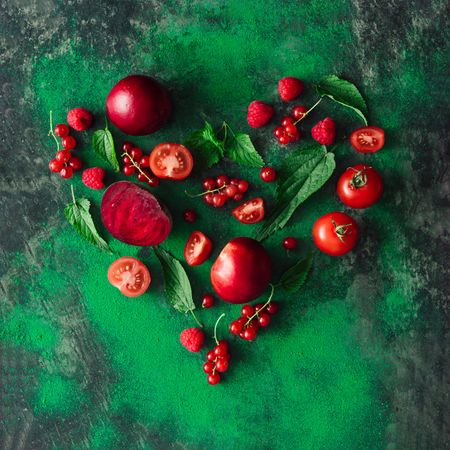 Heart shape made of red healthy food, fruits, and vegetables with green leaves