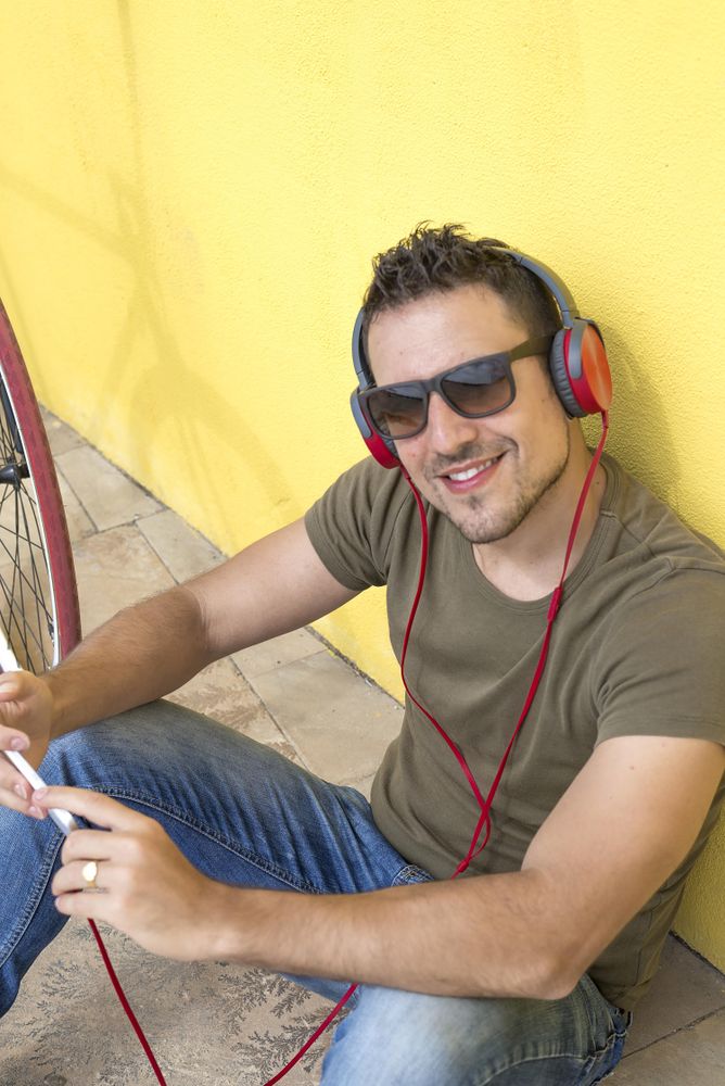 Looking down at happy man with red headphones sitting outside, vertical