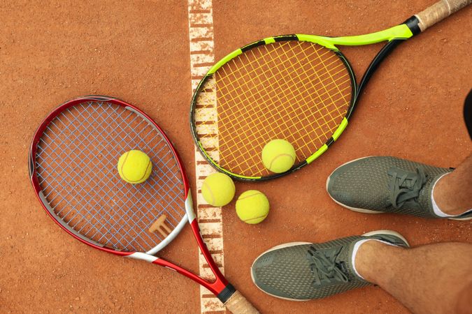 Man feets, rackets and tennis balls on clay court, top view