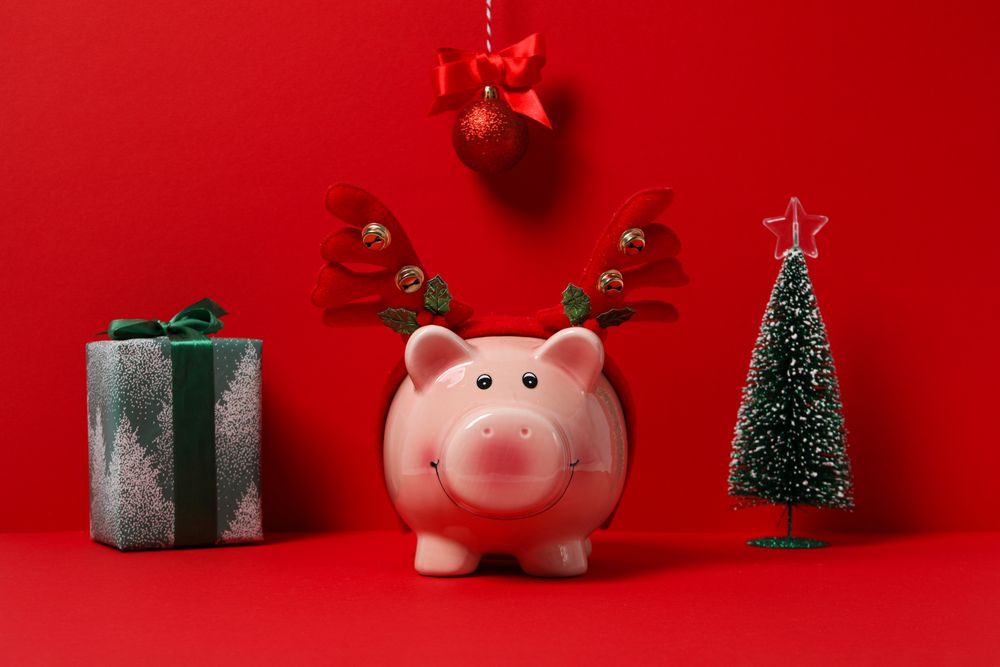Piggy bank with Christmas decor and gift box on red background