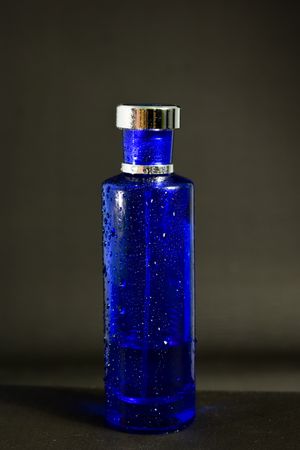 Blue perfume bottle with droplets in grey studio with copy space