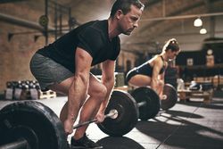 Determined male lifting heavy barbell using body weight