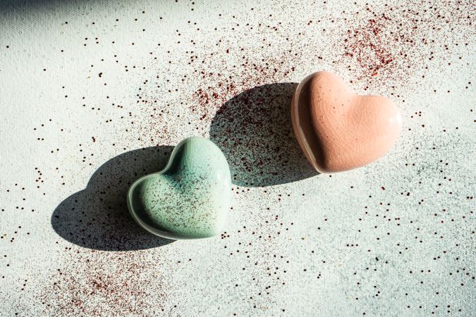 Two pastel ceramic hearts on table with glitter