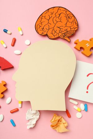 Vertical composition of paper cut out of side view of head with medications and puzzle pieces