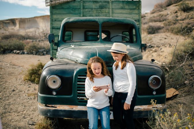 Cheerful girls watching smartphone near abandoned truck