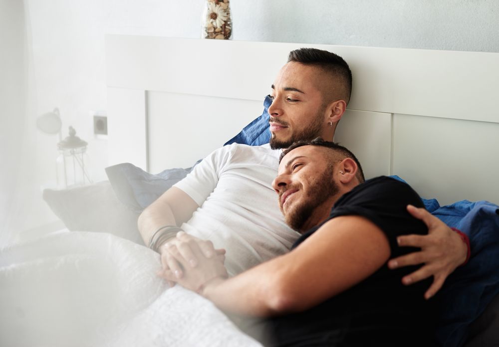 Smiling gay couple hugging on bed