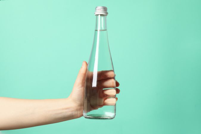 Hand holding tall glass water bottle in green room