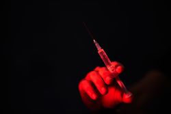 Crop person with syringe in dark room