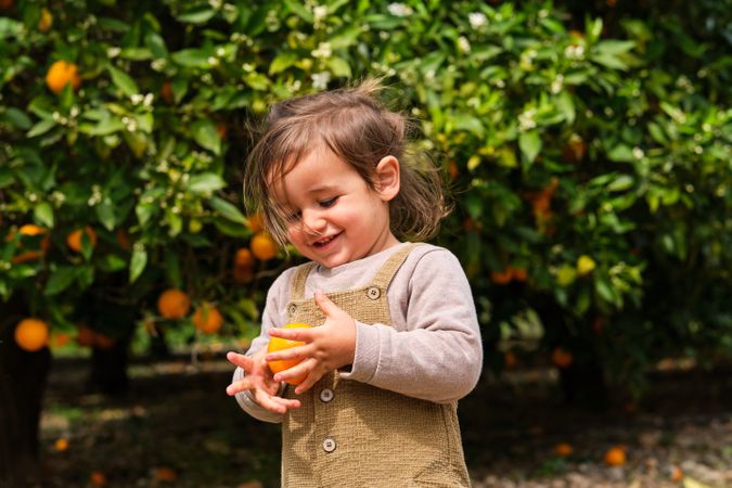 Content boy with fresh orange against trees in garden